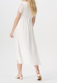 Robe blanche longueur au sol avec manches courtes à volants et détail de taille nouée. Tissu lisse et léger avec une silhouette fluide.