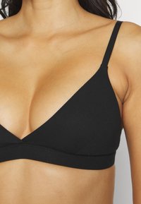 Čierny bralet s trojuholníkovým tvarom, mäkkou rebrovanou textúrou, nastaviteľnými ramienkami a jednoduchým, bezšvíkovým dizajnom.