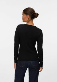 Svart långärmad topp med ribbat mönster och rund halsringning, kombinerad med mörkblå jeans med synliga sömmar och fickor.