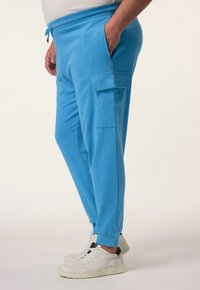 Blaue Baumwoll-Jogginghosen mit elastischem Bund, seitlichen Taschen und gerippten Bündchen, kombiniert mit weißen Sneakern. Mit einem kleinen Markenlogo.