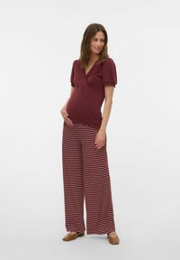 Ensemble de maternité comprenant un haut en maille côtelée bordeaux avec un décolleté en V et des manches bouffantes, associé à un pantalon à jambes larges rayé en bordeaux et blanc.