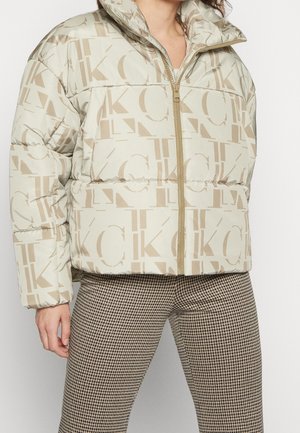 Giacca a vento beige con motivo logo, dotata di colletto alto e chiusura con zip. Indossata con pantaloni a quadri per creare contrasto.
