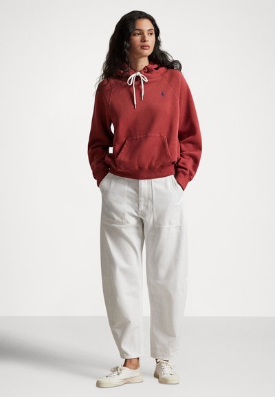 Rødbrun hettegenser med snor, kengurulomme og ribbestrikkede mansjetter, kombinert med ledige hvite bukser og lyse sneakers.