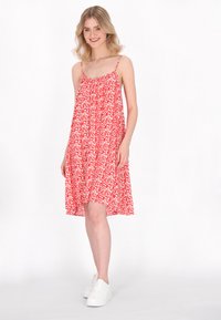 Rochie roșie fără mâneci cu model floral alb, material fluid, decolteu adunat și detaliu pe tivul lateral. Asortată cu adidași albi.