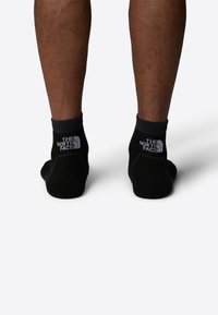 Svarta ankelsockor med ribbad kant och en kontrasterande vit logotyp på baksidan. Slät textur med en tät passform, utformade för komfort.