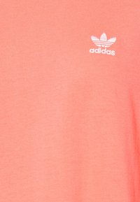 Coral bomulds-t-shirt med det hvide Adidas-logo og ribbet tekstur, der fremhæver et enkelt, klassisk design.