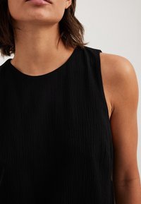 Czarny bezrękawnik z teksturowanej tkaniny i okrągłym dekoltem, z miękką, lekko pomarszczoną powierzchnią i bez widocznych zapięć.