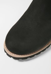 Svart mocka ankelboot med rund tå och kontrasterande beige sömnad. Har en texturerad sula för bra grepp.