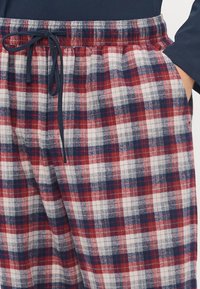 Pantalones de pijama de franela en cuadros rojos y marinos con cintura elástica, cordón y bolsillos laterales. Textura suave y corte holgado.