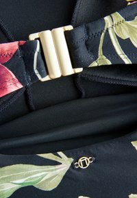 Tessuto nero con un motivo floreale caratterizzato da foglie rosa e verdi. Accessori in metallo dorato fissano il design, aggiungendo un tocco elegante.