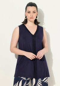 Marineblauwe mouwloze blouse met een V-hals en contrasterende zwarte accenten. Glad materiaal met een ontspannen pasvorm, gecombineerd met gestreepte broek.