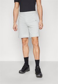 Világosszürke sportos rövidnadrág elasztikus derékpánttal, bal combján egy kis sötét logóval, fekete túrázó cipőkkel és zoknikkal párosítva.