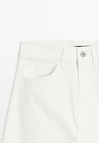 White denim pants with a structured waistband, a front pocket, and a metal button closure. The fabric has a smooth texture.