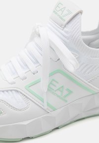 White sneaker with textured knit upper, white laces, and light green Emporio Armani EA7 logo on side and tongue.