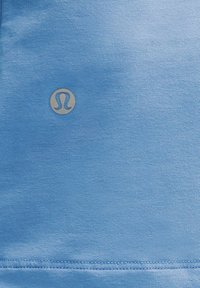 Lichtblauwe sportstof met een gladde textuur en een klein, zilveren logo in het midden. Netjes gestikte randen.