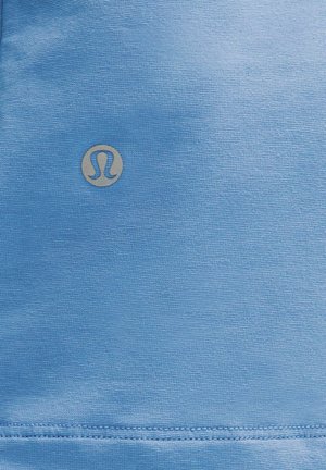 Tessuto atletico azzurro chiaro con una superficie liscia e un piccolo logo argentato al centro. Cuciture pulite lungo i bordi.