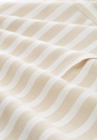 Tissu à rayures horizontales beige et blanc avec une texture lisse, présenté en plis doux sous un éclairage naturel.