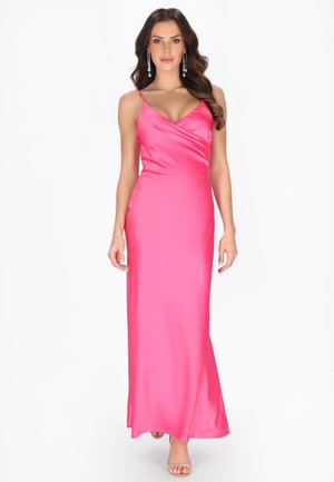 Kvinde iført en lang, lyserød satin kjole med tynde stropper og hængende øreringe, gående fremad på en hvid baggrund.