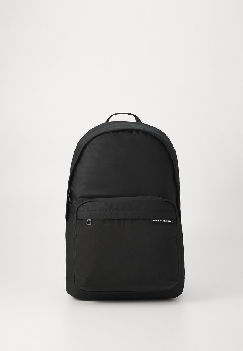 Mochila preta com textura suave, topo arredondado, bolso frontal com fecho e detalhe do logótipo. Feita de material durável, com alças ajustáveis.