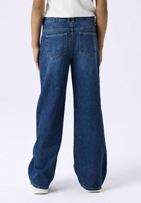 Jean en denim bleu à jambe large avec une taille haute, doté de deux poches arrière et d'une texture lisse. L'ourlet est légèrement effiloché.