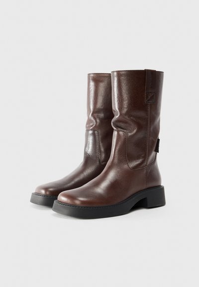 Brown leather knee-high boots with a slightly slouched design, round toe, and a chunky black rubber sole. Features a rear loop for easy wear.