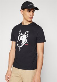 T-shirt en coton noir avec un grand graphique de bull terrier blanc et le texte rouge "HUGO". Coupe ajustée avec des manches courtes et un col rond.