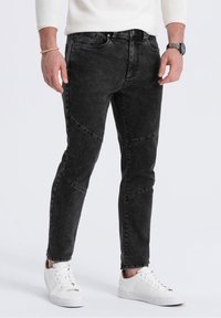 Svarta denimjeans med slim fit, som har unika panelstygn och en blekt textur. I kombination med vita sneakers för kontrast.