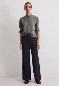 Oversized, collared shirt in textured grey fabric, paired with high-waisted, wide-leg black trousers. Smooth texture and minimalistic design.