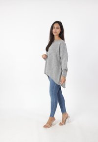 Grijze gebreide trui met verlaagde schouders, een ronde zoom en ribgebreide manchetten, gecombineerd met blauwe skinny jeans en transparante hakken sandalen.