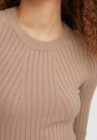 Ljusbrun ribbad stickad topp med rund halsringning, med vertikala ränder och en mjuk textur. Ingen synlig hårdvara eller detaljer.
