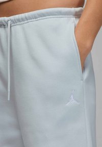 Jasnoniebieskie spodnie dresowe wykonane z miękkiego materiału, wyposażone w elastyczny pas i boczne kieszenie, z białym haftowanym logo na udzie.