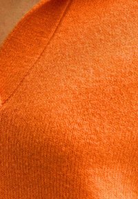 Maglione a V in un vivace arancione, realizzato in tessuto lavorato a maglia, con una finitura morbida e cuciture visibili lungo il colletto.