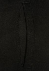 Zwart gebreide stof met een zakopening aan de zijkant, met een gladde textuur en minimale naden, wat de eenvoudige ontwerp benadrukt.