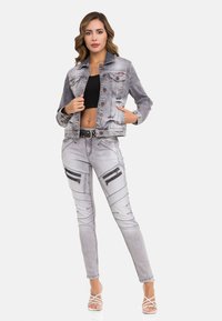 Jeansjack en een aansluitende broek in lichtgrijs met ritszakken, opvallende stikdetails en een zwarte riem, gedragen met een zwart crop top.