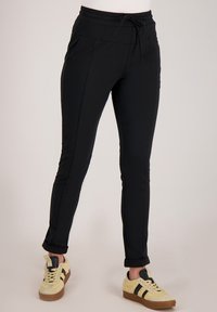 Zwarte atletische broek met een trekkoord in de taille, taps toelopend ontwerp, zijzakken en opgerolde boorden, gecombineerd met lichtgekleurde sneakers.