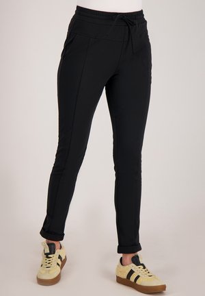 Zwarte atletische broek met een trekkoord in de taille, taps toelopend ontwerp, zijzakken en opgerolde boorden, gecombineerd met lichtgekleurde sneakers.