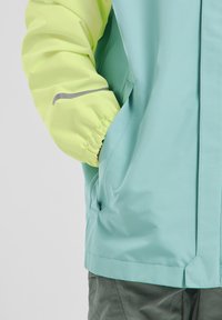 Chaqueta ligera con cuerpo en color verde menta y mangas amarillas neón. Presenta puños elásticos, bolsillos y Acabados reflectantes. Textura suave.