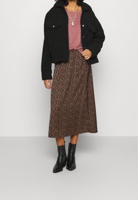 Zwarte fleecejack met voorzakken, roze t-shirt en bruine gestreepte midi-rok. G gedragen met zwarte enkellaarsjes.