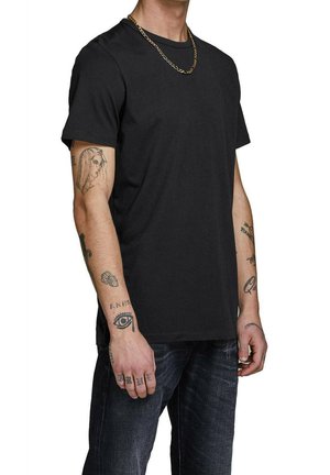 Camiseta de algodón negra con cuello redondo, mangas cortas y dobladillo recto. Destaca un collar de cadena dorada y varios tatuajes en los brazos.