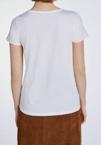 Camiseta blanca de manga corta, material de algodón suave, escote redondeado, dobladillo ligeramente curvado, combinada con una falda de ante marrón.