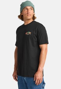 Black cotton t-shirt featuring a colorful embroidered "Billabong" logo on the chest. Short sleeves and a classic crew neck design.