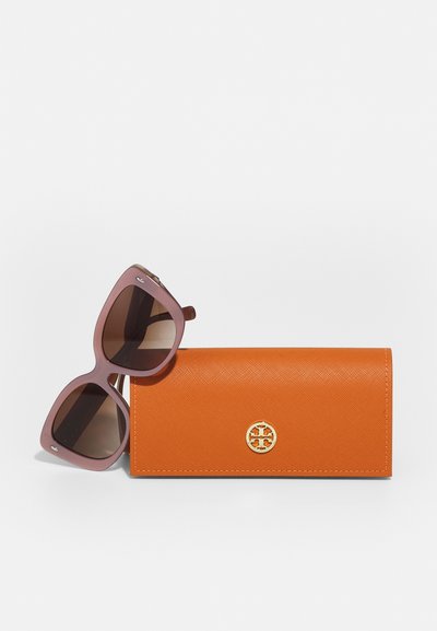 Rosa übergroße Sonnenbrille mit braunen Gläsern neben einem orangefarbenen, strukturierten Etui mit einem goldenen Logo-Akzent.