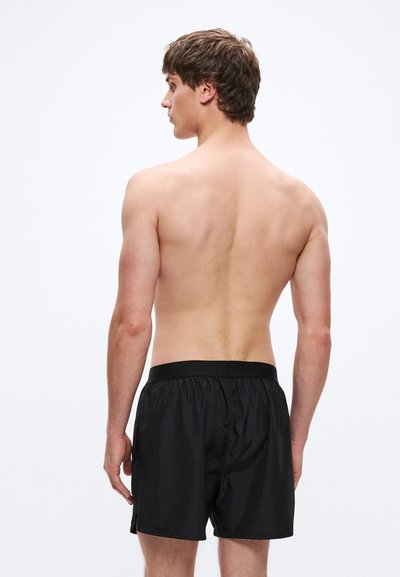 Fekete úszónadrág, könnyű anyagból készült, elasztikus derékpánttal és laza szabással, hátulnézetben.