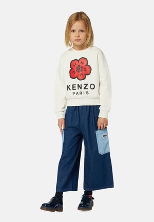 Sweatshirt blanc avec un graphique de fleur rouge et le texte "KENZO PARIS" ; culottes en denim bleu loose avec des accents de poches bleu clair ; chaussures noires brillantes.