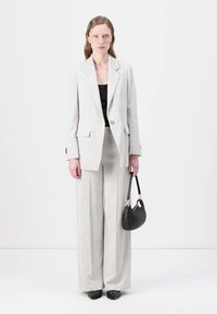 Lys grå stribede jakkesæt med en skræddersyet blazer og vide bukser. Sort top og håndtaske. Sorte sko. Enkel design med minimale accenter.