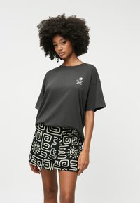 Black oversized t-shirt with "Vacation Club" graphic and short patterned skirt with white abstract designs on a black background.