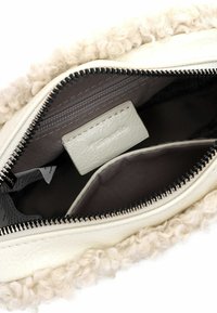 Interno di una borsa in pelle bianca con rivestimento morbido e texturizzato color crema, una tasca con zip e una piccola etichetta. Presenta dettagli della cerniera nera e un tessuto a contrasto.