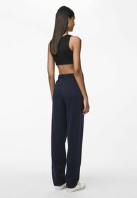 Zwarte cropped tanktop en marineblauwe wijde sweatpants met een elastische tailleband, gecombineerd met witte sneakers. Gladde stofstructuur zichtbaar.