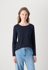 Marineblaue Langarmbluse aus weichem Material mit rundem Halsausschnitt, kombiniert mit hellblauen Jeans in lockerer Passform.