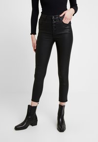 Černé kalhoty z umělé kůže s vysokým pasem, tvarovaným střihem, pěticí knoflíků vpředu a délka ke kotníkům, doplněné černými kotníkovými botami na podpatku.